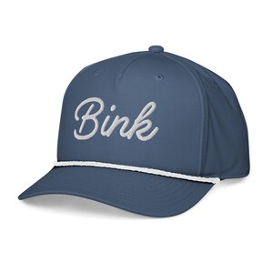 May include: A navy blue baseball cap with the word "Bink" embroidered in white script. The cap features a white rope detail along the brim and a curved visor. The hat is a classic style.