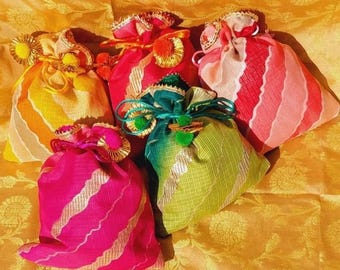 May include: A collection of colorful, decorative drawstring bags. The bags are in shades of yellow, pink, red, and green, with striped and patterned designs. Each bag is adorned with decorative trim and bows.