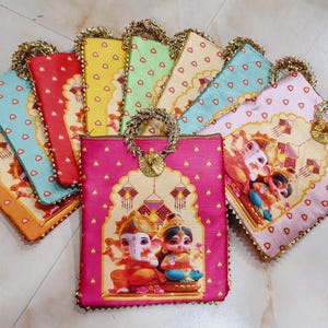 May include: A selection of vibrant fabric bags with gold handles. Each bag displays a unique colour and design, including images of deities. The bags are embellished with gold trim and arranged in a fan-like pattern.
