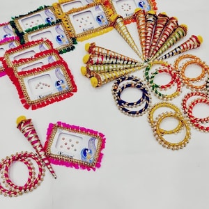May include: An assortment of colorful Indian decorative items, including framed stickers with peacock designs, decorative cones, and beaded bangles. The frames have the word "Kusum" printed on them. The items are arranged on a white surface.