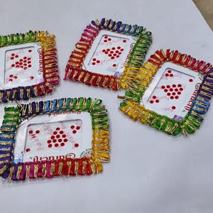 May include: Four square, colorful frames with a decorative, fringed border. Each frame has a white interior with a pattern of red dots. The frames are arranged on a white surface.