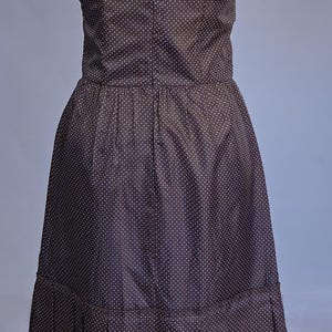 May include: A strapless, knee-length dress in a dark brown fabric with a white polka dot pattern. The dress features a fitted bodice and a pleated skirt. The dress is displayed on a mannequin.