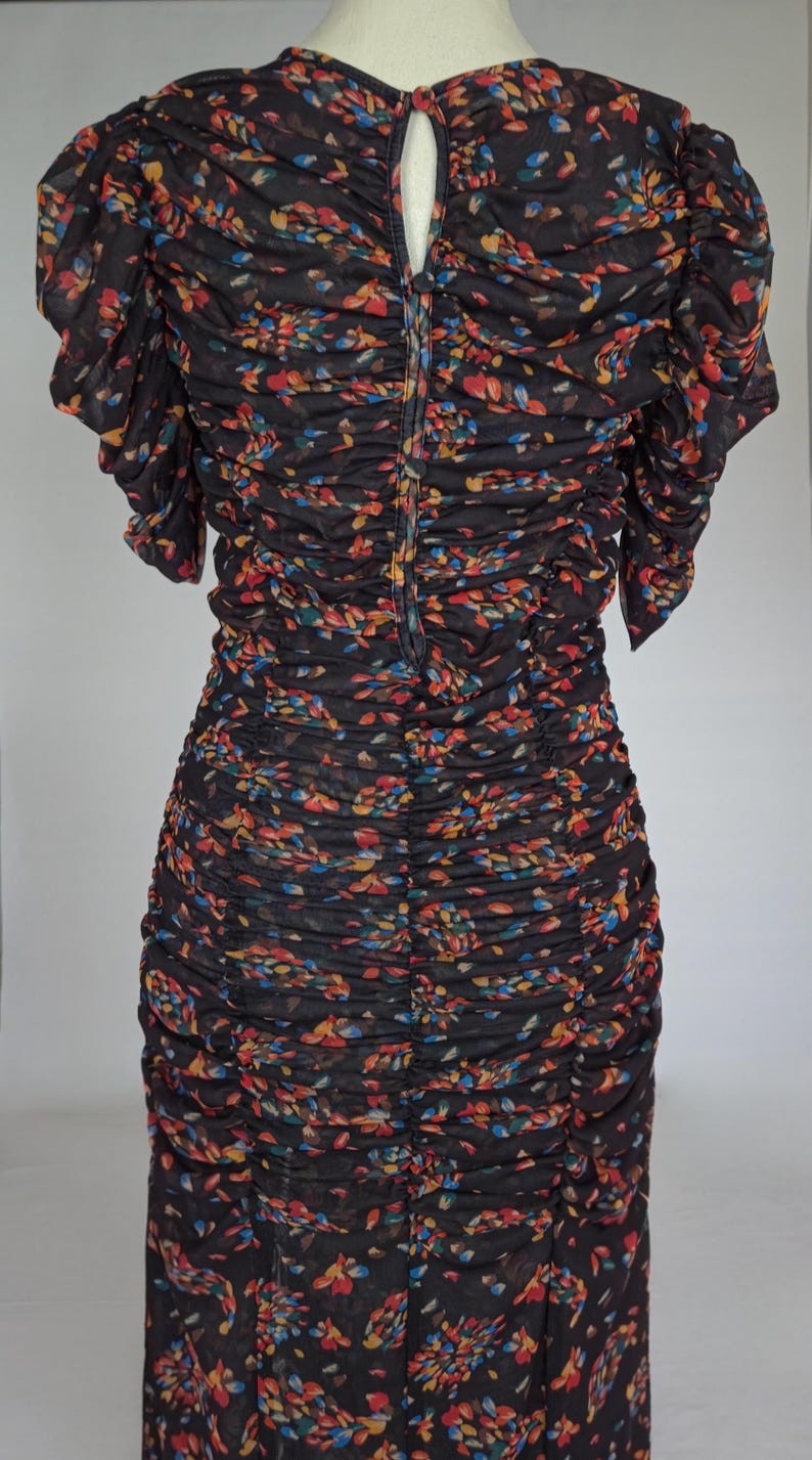 May include: A black dress with a floral pattern in red, yellow, and blue. The dress has a ruched design and short sleeves. The back of the dress has a keyhole opening and a zipper closure.