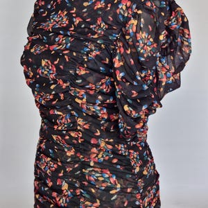 May include: Black dress with a floral pattern in red, yellow, blue, and green. The dress features a round neckline and short, ruffled sleeves. The fabric is gathered throughout the bodice and skirt.