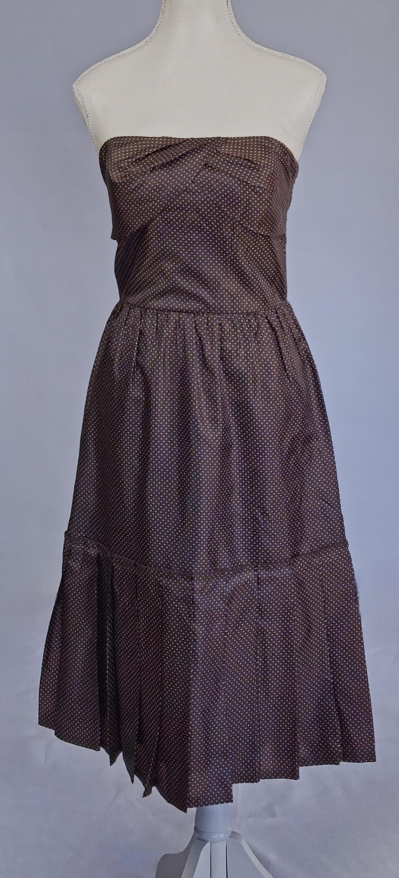 May include: A dark brown, knee-length dress with a strapless design and a pattern of small, light-coloured dots. The dress has a fitted bodice, a gathered waist, and a tiered skirt.
