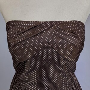 May include: A strapless brown dress with white polka dots. The bodice has a twisted design, and the skirt is gathered. The dress is displayed on a mannequin.