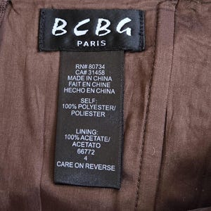 May include: A close-up shot of a brown garment featuring a black label with "BCBG PARIS" printed on it. The label provides fabric details and care instructions. The garment is made of polyester and acetate.