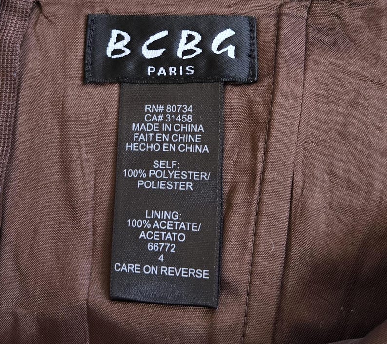May include: A close-up shot of a brown garment featuring a black label with "BCBG PARIS" printed on it. The label provides fabric details and care instructions. The garment is made of polyester and acetate.