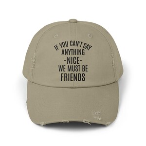 May include: A beige baseball cap with a distressed finish. The cap displays the text "IF YOU CAN'T SAY ANYTHING -NICE- WE MUST BE FRIENDS" in black. It has a curved peak and an adjustable strap for a comfortable fit.