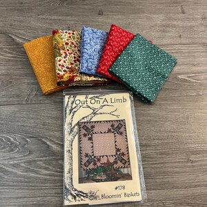 May include: A collection of folded fabric squares in various colors, including gold, floral, blue, red, and green, arranged near a pattern titled "Out On A Limb" with the text "Bloomin' Baskets". The fabrics appear to be cotton.