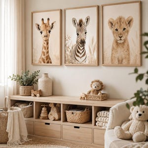 May include: Three framed wall art prints featuring a giraffe, a zebra, and a lion cub, each set against a neutral background with tall grasses. The prints are displayed in light wood frames above a wooden storage unit with baskets and toys.