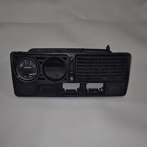 Puede incluir: Un panel de consola central de salpicadero de coche negro que presenta un indicador circular con el texto CNSPEED, una carcasa de indicador circular vacía, una rejilla de ventilación rectangular y varias ranuras para interruptores.