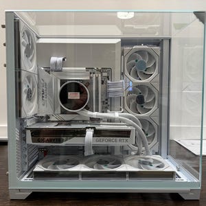 May include: A white computer case with a glass panel showcasing internal components. The components include a Gigabyte GeForce RTX graphics card, multiple fans, and a liquid cooling system. The case is on a white base.