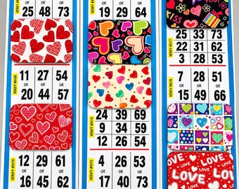Può includere: Tre cartelle di bingo verticali con bordi blu, ciascuna contenente diverse griglie numerate e segnapunti rettangolari colorati con motivi a cuore, il testo I LOVE YOU e varie forme geometriche in design rossi, neri e multicolori.