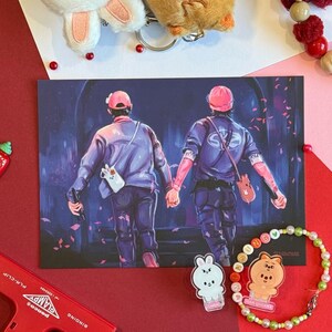 K&ouml;nnte beinhalten: Eine Sammlung von Accessoires, darunter Pl&uuml;sch-Schl&uuml;sselanh&auml;nger, ein Armband und ein roter Tacker. Die Schl&uuml;sselanh&auml;nger sind in Form eines wei&szlig;en Hasen und eines braunen B&auml;ren gehalten. Eine Postkarte zeigt zwei Figuren, die sich an den H&auml;nden halten. Das Armband hat bunte Perlen.