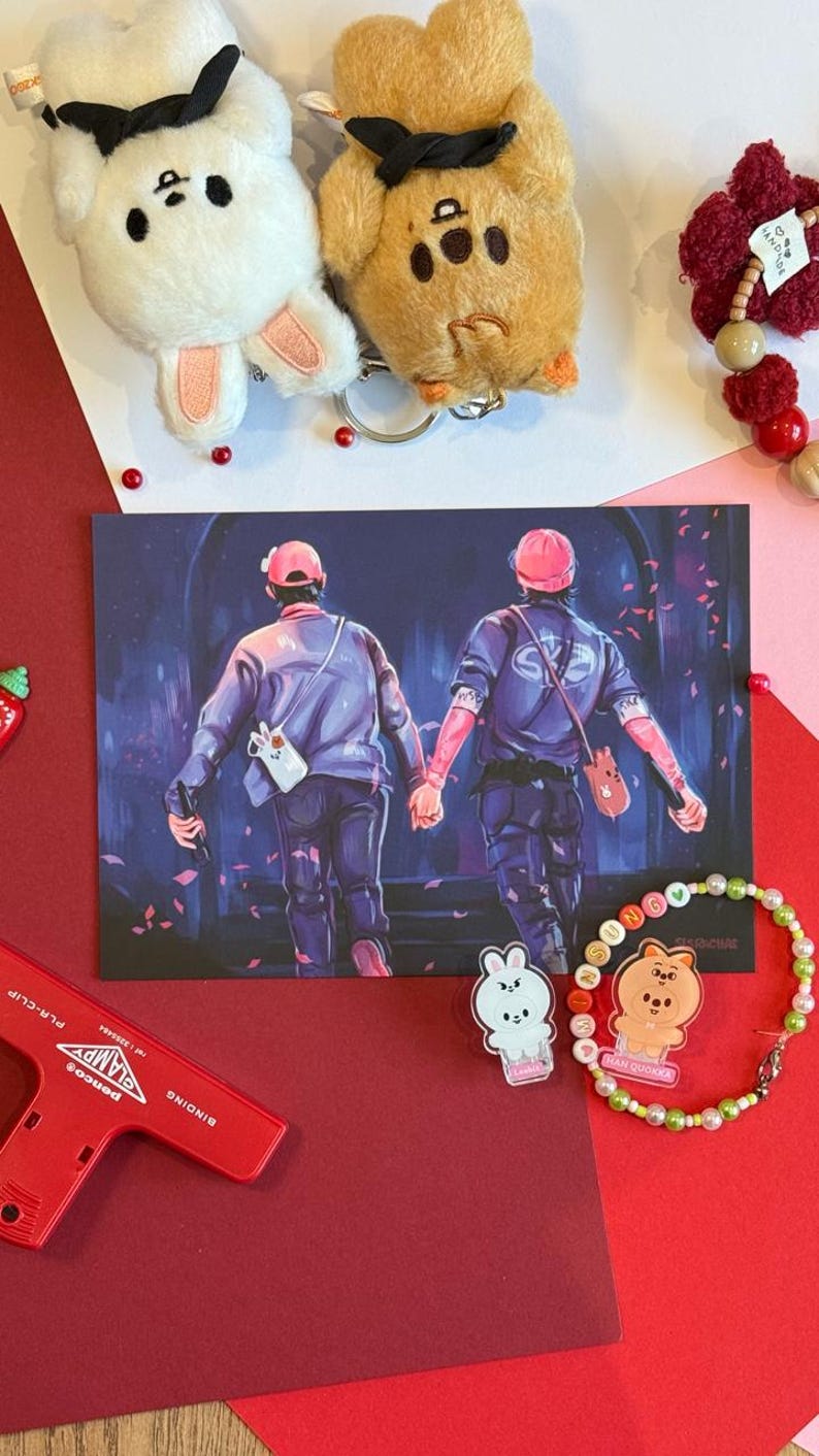 K&ouml;nnte beinhalten: Eine Sammlung von Accessoires, darunter Pl&uuml;sch-Schl&uuml;sselanh&auml;nger, ein Armband und ein roter Tacker. Die Schl&uuml;sselanh&auml;nger sind in Form eines wei&szlig;en Hasen und eines braunen B&auml;ren gehalten. Eine Postkarte zeigt zwei Figuren, die sich an den H&auml;nden halten. Das Armband hat bunte Perlen.