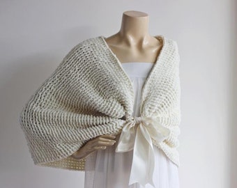 May include: A white knitted shrug with a satin ribbon tie. The shrug is made of a soft, lightweight yarn and has a relaxed fit.