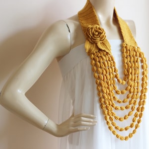May include: A yellow crocheted necklace with a flower accent. The necklace is made of multiple strands of crocheted beads.