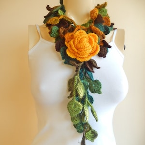 May include: A crocheted scarf with a large yellow flower and green leaves. The scarf is made of yarn and is a beautiful accessory for any outfit.