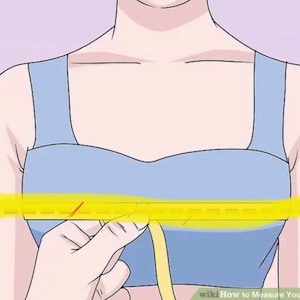 May include: A woman wearing a light blue bra with a yellow measuring tape around her chest. The tape measure is being held by her right hand.