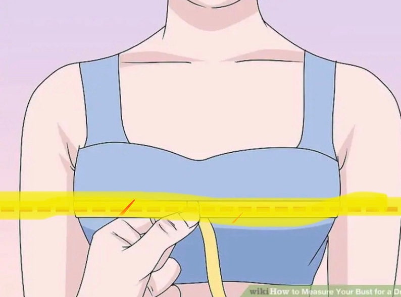 May include: A woman wearing a light blue bra with a yellow measuring tape around her chest. The tape measure is being held by her right hand.