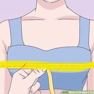 May include: A woman wearing a light blue bra with a yellow measuring tape around her chest. The tape measure is being held by her right hand.