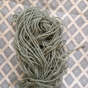 May include: A skein of sage green yarn, labeled "138 SAGE GREEN", on a white and gray patterned surface.