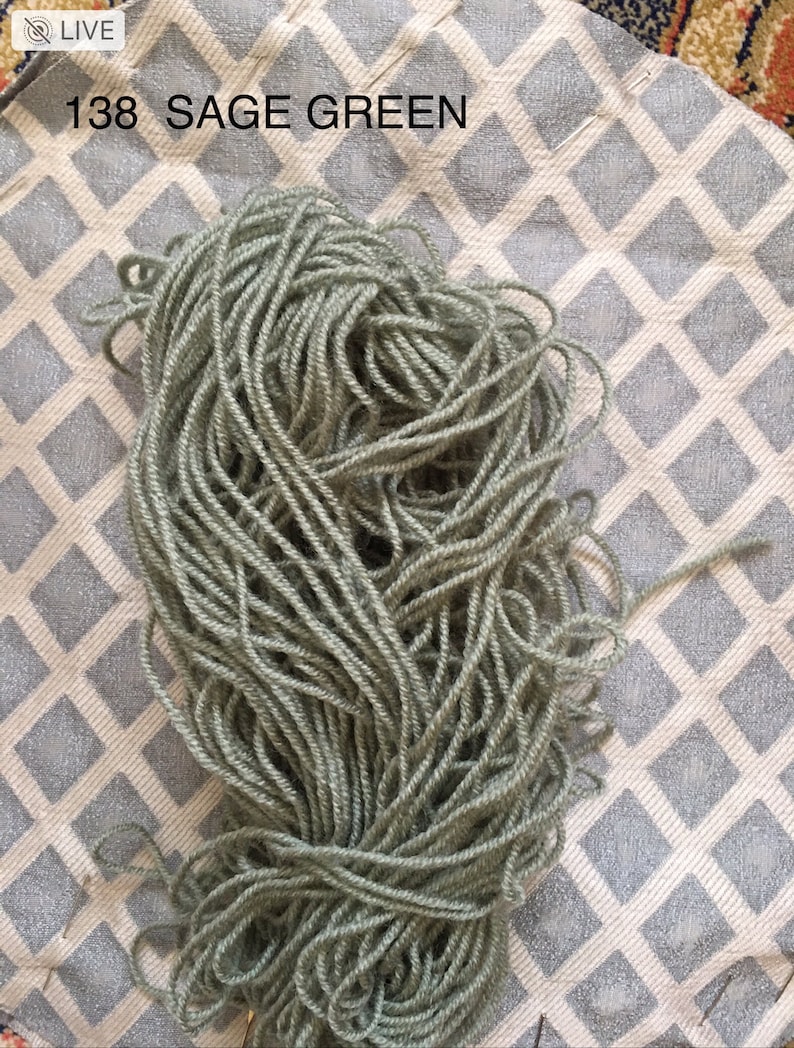 May include: A skein of sage green yarn, labeled "138 SAGE GREEN", on a white and gray patterned surface.