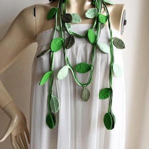 May include: A long, multi-strand necklace made of crocheted green leaves. The necklace is worn by a mannequin with a white dress.