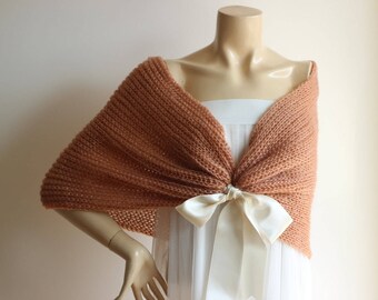 May include: A knitted shawl in a light brown color with a white satin ribbon tied in a bow at the front.