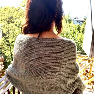 May include: A sage green knitted sweater with a loose, oversized fit. The sweater has a wide neckline and long sleeves.