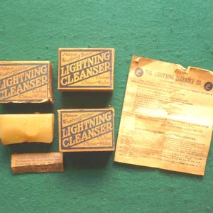 May include: An assortment of vintage Lightning Cleanser products, including three boxes, a bar of soap, and a small rectangular item with text. The boxes are labeled "Lightning Cleanser" with the text "Makes Washing Easy Clothes Clear-White."