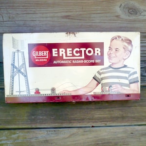 May include: Vintage Gilbert Erector Set box with a red and white design. The box features the text "Gilbert Erector" and "Automatic Radar-Scope Set." The image includes a smiling boy and a diagram of a radar tower.