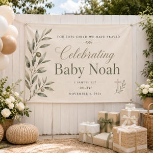 Op de afbeelding: Een rechthoekige, crèmekleurige stoffen banner met een illustratie van een groene olijftak aan de linkerkant en een kruis aan de rechterkant. De tekst luidt: FOR THIS CHILD WE HAVE PRAYED, Celebrating Baby Noah, 1 SAMUEL 1:27, NOVEMBER 8, 2026.