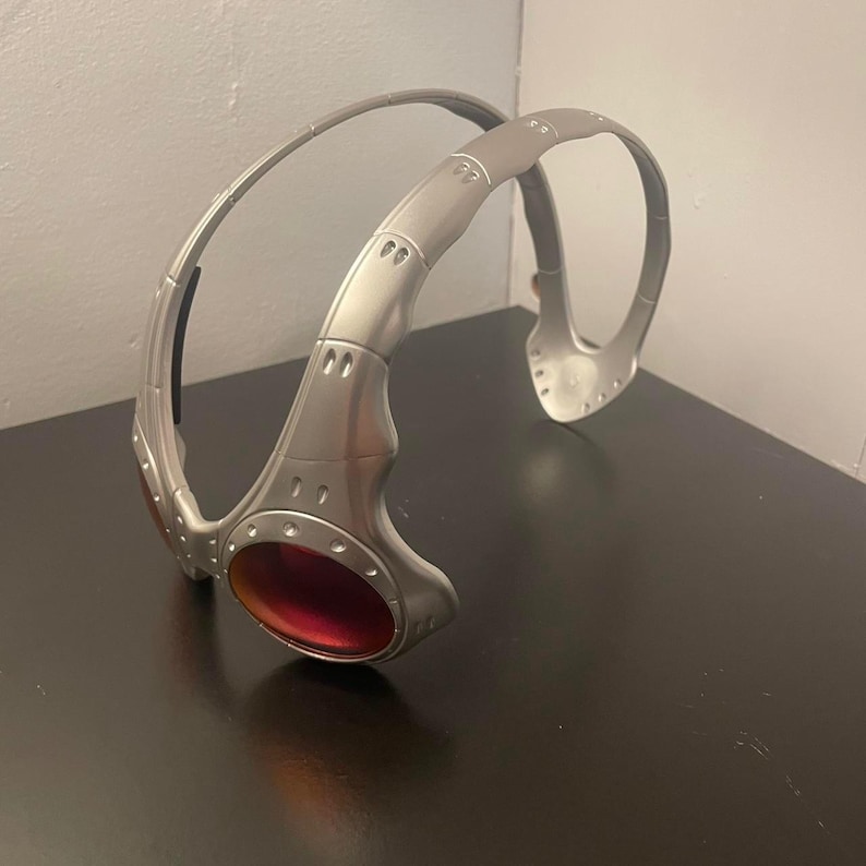 May include: Silver-colored sports sunglasses with a wraparound design. The sunglasses have a thick frame and red-tinted lenses. The design features a curved top bar and a sculpted nose bridge.