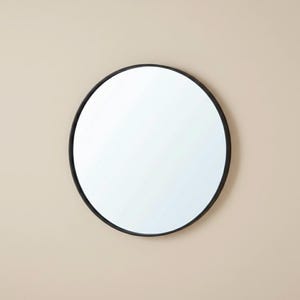 May include: A circular mirror with a black frame. The mirror is positioned centrally, reflecting the surroundings. The frame is a thin, solid black. The background is a plain, neutral colour.