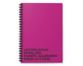 Puede incluir: Un cuaderno magenta con espiral y texto negro: "GETTING STUFF DONE, ONE PASSIVE-AGGRESSIVE EMAIL AT A TIME." El cuaderno tiene una encuadernación en espiral negra.