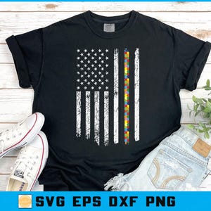 May include: Black t-shirt with a distressed American flag design, incorporating a vertical stripe of colourful puzzle pieces. The shirt has the text "SVG EPS DXF PNG" at the bottom. White trainers and denim shorts are also visible.