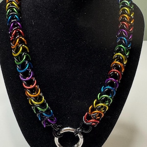 May include: A chainmail necklace constructed from interlocking anodized aluminum rings in a vibrant rainbow spectrum of red, orange, yellow, green, blue, and purple, accented with black rings and a central polished silver-tone metal O-ring clasp.