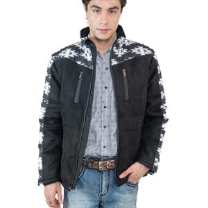 May include: Black suede jacket with white and black geometric pattern on the shoulders and sleeves. The jacket has a zipper closure and two front pockets. The person is wearing a gray button-down shirt and blue jeans.
