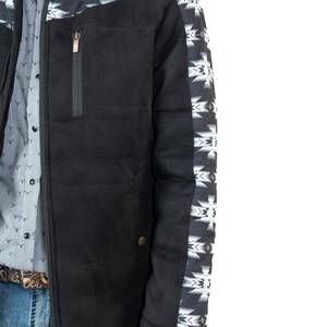 May include: Black jacket with a geometric pattern on the shoulders and sleeves. The jacket has a high collar, a zippered chest pocket, and a button closure. The jacket is worn over a patterned shirt and blue jeans.