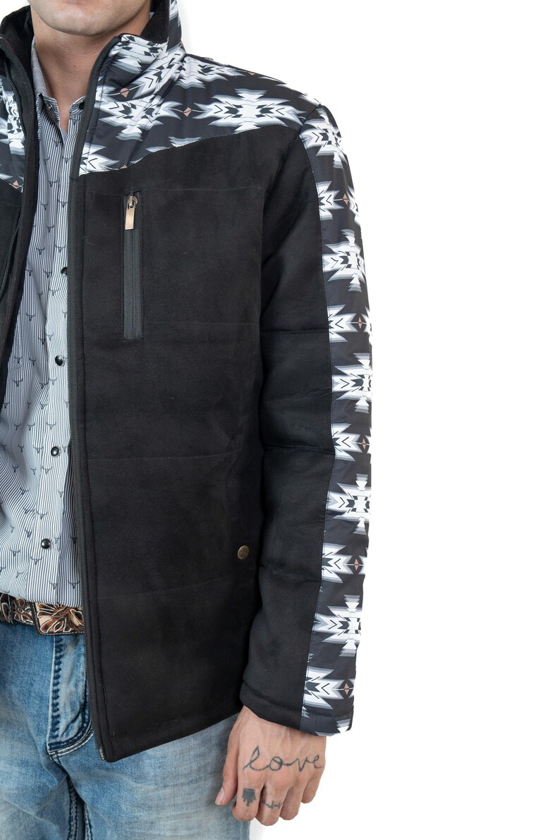 May include: Black jacket with a geometric pattern on the shoulders and sleeves. The jacket has a high collar, a zippered chest pocket, and a button closure. The jacket is worn over a patterned shirt and blue jeans.