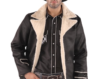 May include: A black cowboy hat sits atop a black jacket with cream-colored faux fur lining. The jacket is worn over a black button-down shirt with white trim. The person is wearing blue jeans and a brown belt with a decorative buckle.