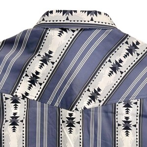 May include: Close-up of a blue and white patterned shirt. The shirt features vertical blue stripes with white and black geometric designs. The collar and yoke are visible, showcasing the detailed pattern.