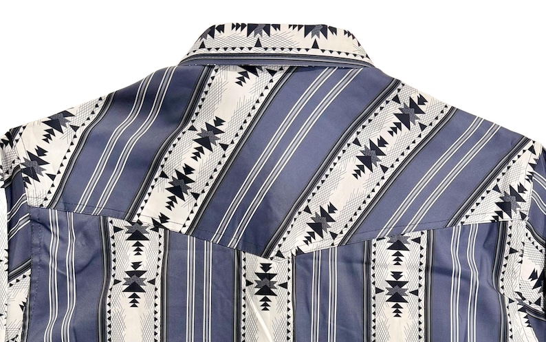 May include: Close-up of a blue and white patterned shirt. The shirt features vertical blue stripes with white and black geometric designs. The collar and yoke are visible, showcasing the detailed pattern.