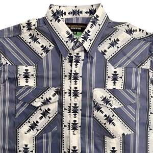 May include: A blue and white patterned button-up shirt with a Western design. The shirt features vertical stripes and geometric patterns on the pockets, collar, and yoke. The text "THE AMERICAN WEST - BORN IN USA" is visible on the collar.