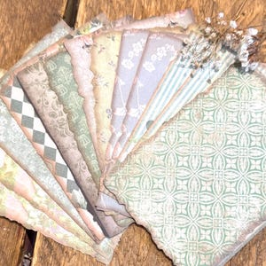 Op de afbeelding: Een verzameling papieren ephemera in vintage-stijl met verschillende patronen en kleuren, waaronder bloemen-, geometrische en gestreepte ontwerpen. De randen zijn geschulpt en verweerd, met een accent van gedroogde bloemen.