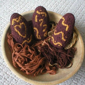 May include: Three brown yarn-wrapped eggs with gold embroidery designs in a wooden bowl with brown yarn.