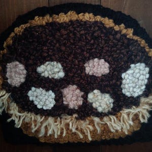 May include: A brown and tan hand-stitched rug with a circular design featuring white and pink circles. The rug has a fringe border.