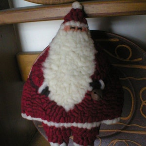 May include: A red and white felt Santa Claus ornament with a white beard and a red hat. The ornament is holding a small bell in its right hand.